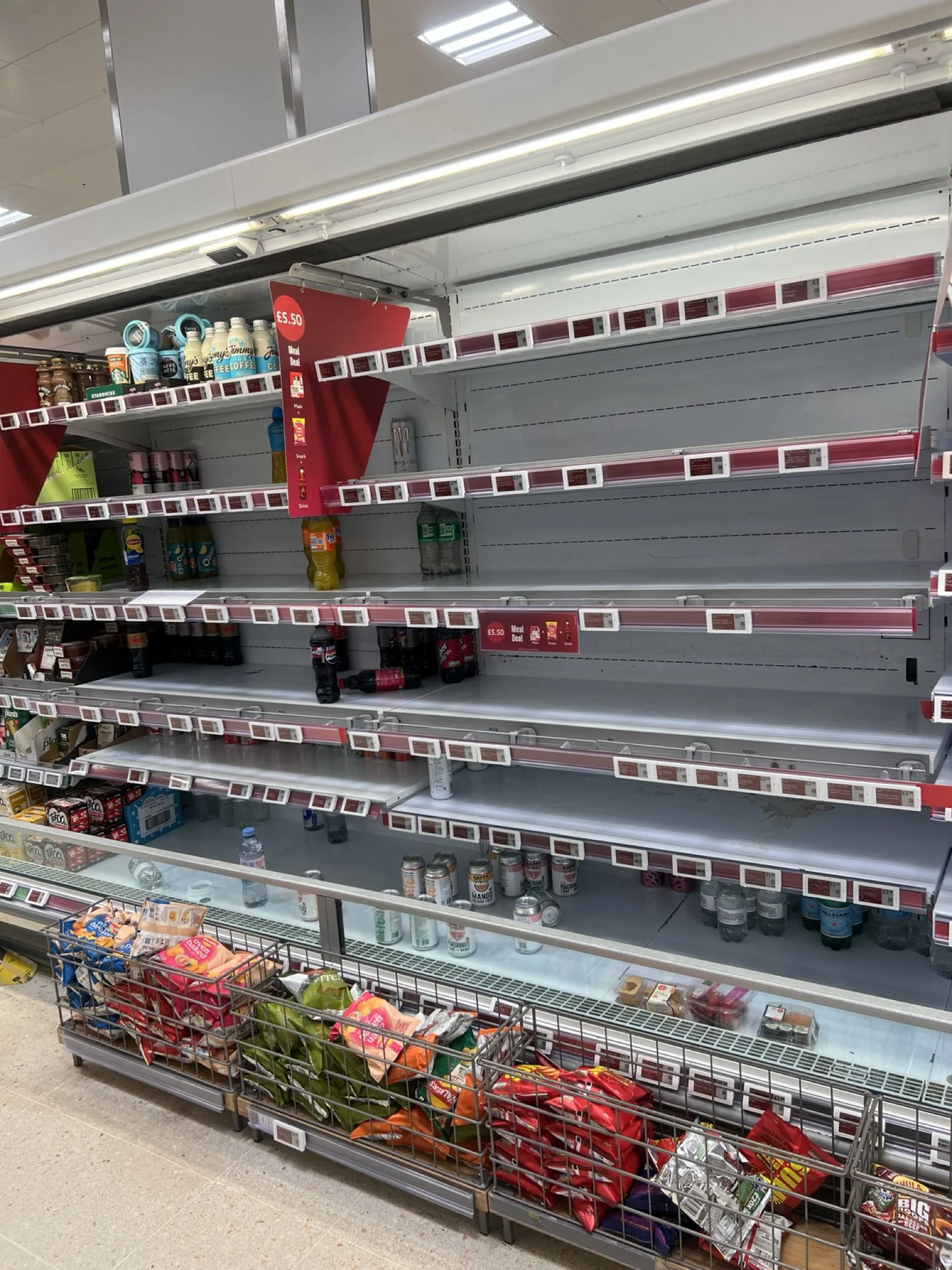 Supermarket fridge shelves with multiple rows almost empty of stock